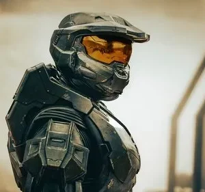 Guerreiro blindado futurista em armadura cinza-escura, visor laranja/dourado. Fundo com estruturas difusas em tons terrosos. Clima sério e sci-fi.