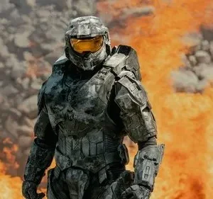 Pôster: Um soldado em armadura cinza futurista com visor amarelo em pé em meio a chamas e fumaça. Cena de ação e destruição.