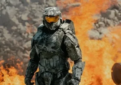 Pôster: Um soldado em armadura cinza futurista com visor amarelo em pé em meio a chamas e fumaça. Cena de ação e destruição.