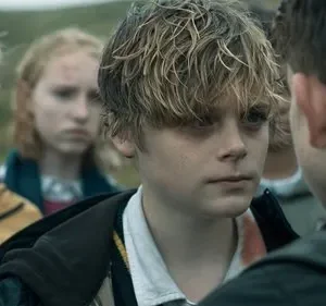 Um jovem de cabelo desgrenhado encara outro. Ao fundo, outros adolescentes com expressões sérias e pequenos ferimentos no rosto.