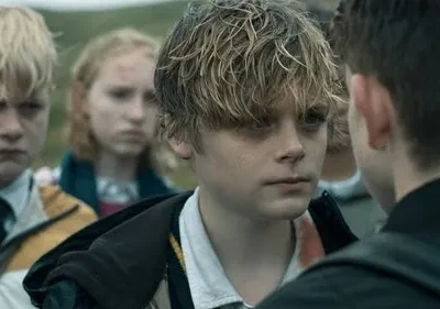 Um jovem de cabelo desgrenhado encara outro. Ao fundo, outros adolescentes com expressões sérias e pequenos ferimentos no rosto.