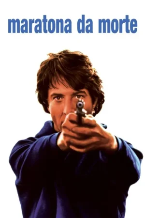 Homem com cabelo castanho e camisa azul escura aponta uma arma para a câmera, com olhar intenso, em fundo branco.