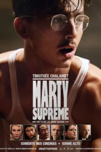 Close-up de um homem jovem,de óculos e bigode,em camiseta branca,com olhar intenso e suor no rosto. Fundo escuro.