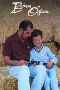 Pai e filho sentados em fardos de feno. O homem olha para o menino que sorri,segurando uma câmera antiga. Cena terna.