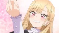 Garota anime loira, olhos rosa brilhantes, sorri amplamente e cora, levantando algo. Fundo rosa com padrões. Clima alegre.