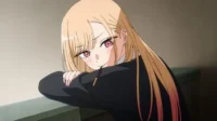 Jovem anime loira de olhos rosa, bochechas coradas, comendo um palito de chocolate. Ela está apoiada e exibe um olhar tímido.
