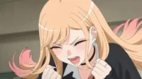 Jovem mulher anime loira com pontas rosa, piercings e choker. Ela sorri extasiada de olhos fechados, punhos cerrados e bochechas coradas.
