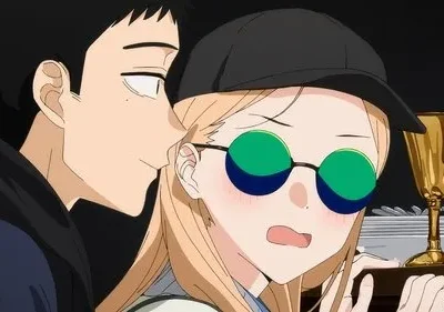 Um homem sussurra para uma mulher loira de boné e óculos de sol, que está corada e com expressão surpresa. Taças douradas ao fundo.