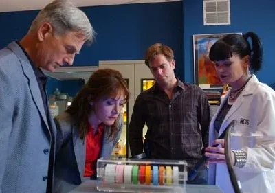 Quatro investigadores, incluindo uma cientista, num laboratório, olham focados um objeto transparente com faixas coloridas.