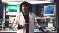 NCIS:Investigação Naval – T01E17:A Verdade Está Lá Fora 6 Mulher de cabelo preto com visual alternativo,em jaleco de laboratório,cercada por equipamentos científicos. Segura um objeto.