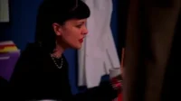 NCIS:Investigação Naval – T01E18:Sem Sigilo 5 Mulher de cabelo escuro com franja,batom vermelho,colar de pérolas. Ela olha para a direita em cena escura com uma bebida.
