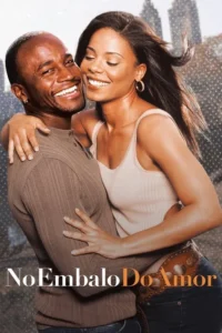 Casal negro sorridente e abraçado em primeiro plano. Ela fecha os olhos feliz,ele olha para a câmera. Prédios desfocados ao fundo.