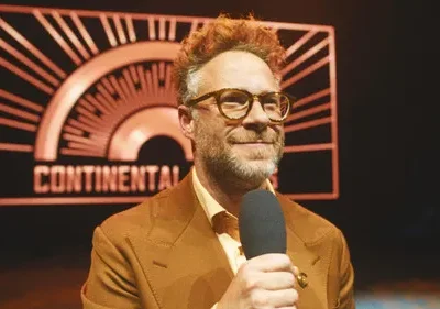 Homem ruivo sorridente de óculos e microfone, em terno marrom. Ao fundo, letreiro CONTINENTAL laranja em estilo art deco.