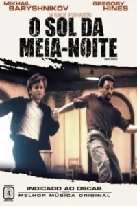 Dois homens dançam em um salão. Um jovem de jaqueta preta e camisa branca;outro,barbudo de camisa marrom. Cena dinâmica.