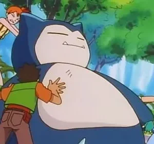 Três jovens lutam para mover uma criatura azul gigante adormecida. Dois garotos e uma garota empurram e puxam em uma floresta.