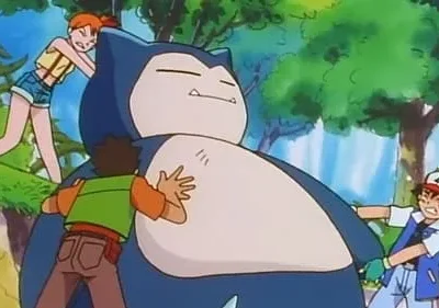 Três jovens lutam para mover uma criatura azul gigante adormecida. Dois garotos e uma garota empurram e puxam em uma floresta.