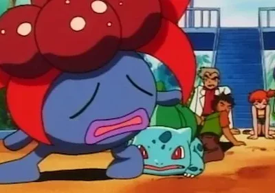 Criatura azul gigante angustiada e outra verde caída no chão. Cinco humanos, incluindo um homem de jaleco, observam preocupados.