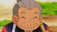 Personagem de anime idoso e feliz,com cabelo grisalho e rosto enrugado,sorri com os olhos fechados. Veste roupa azul e vermelha,em fundo natural.