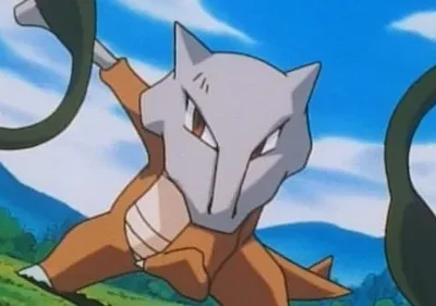 Criatura marrom com máscara de caveira cinza, segurando um objeto verde escuro. Em pose de ataque num campo gramado sob céu azul.