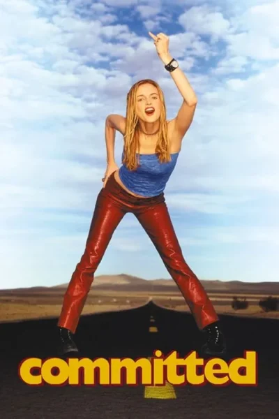 Mulher loira em top azul e calças vermelhas, com o dedo médio levantado, posa de forma desafiadora em uma estrada deserta sob um céu vasto.