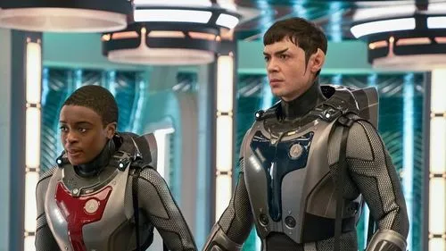 Star Trek:Strange New Worlds – T01E02:Filhos do Cometa 1 Dois tripulantes em trajes futuristas em uma nave espacial. Um homem com orelhas pontudas e um jovem negro olham atentos.