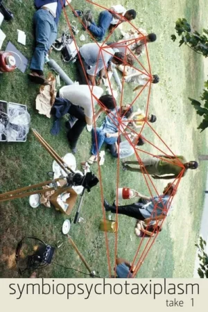 Grupo de pessoas na grama, interligadas por um emaranhado de cordas vermelhas. Equipamentos de câmera próximos. Clima intrigante.
