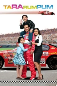 Família sorrindo em pista de corrida. Pai piloto de macacão vermelho com filho nos ombros,filha e esposa ao lado. Carro de corrida vermelho e arquibancadas ao fundo.