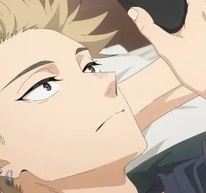 Jovem de cabelo loiro espetado e piercings deitado, olhando para cima com expressão pensativa. Segura um objeto preto próximo à cabeça.