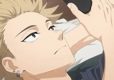 Jovem de cabelo loiro espetado e piercings deitado, olhando para cima com expressão pensativa. Segura um objeto preto próximo à cabeça.