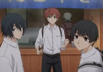 Três jovens, dois com cabelo preto e um ruivo ao centro, estão à frente de uma loja. Vestem camisas brancas, com expressões mistas.