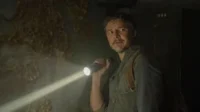 Homem barbudo, tenso, ilumina parede com crescimentos orgânicos em ambiente escuro, número 944.