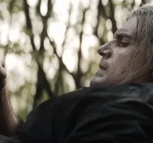 Homem de cabelos grisalhos e suado olha um frasco escuro na mão, com árvores borradas ao fundo. Clima intenso.