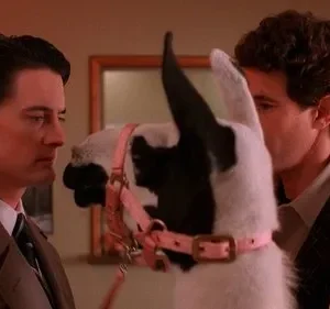 Dois homens e uma lhama com arreio rosa em um ambiente com luz avermelhada. O clima é surreal e peculiar.