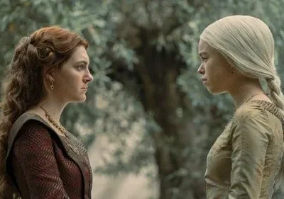 Duas mulheres jovens, uma de cabelo ruivo e outra loira platinada, se encaram tensas em um jardim. Vestes medievais.