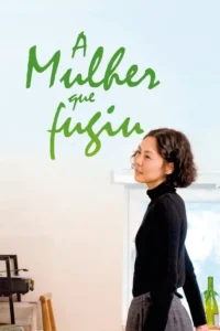 Mulher de cabelo curto e cacheado, blusa preta, com olhar calmo e leve sorriso. Em um quarto claro e arejado com janela.