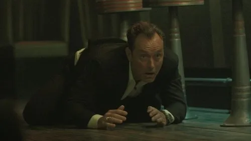 Black Rabbit – T01E06:Se deu bem 1 Homem de terno escuro rasteja no chão,olhando assustado para a frente em um ambiente escuro com colunas metálicas.