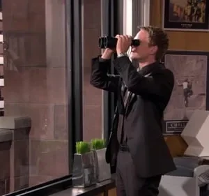 Homem de terno escuro e óculos escuros olha através de binóculos pela janela de um apartamento, observando prédios da cidade.