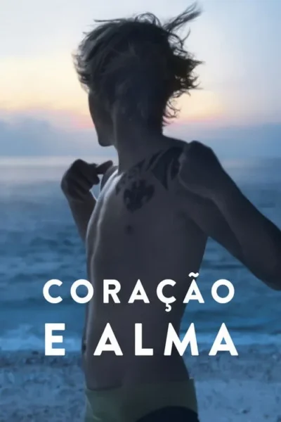 Jovem de costas, sem camisa e com tatuagens no ombro, na praia ao pôr do sol, olhando o mar. Clima sereno.