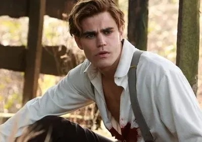 Homem de cabelo castanho claro, camisa branca suja de sangue e suspensórios, olha tenso num cenário rústico de madeira.
