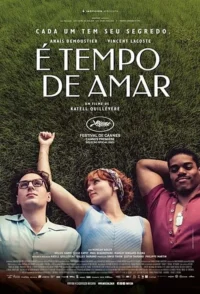 Três jovens,um de óculos,uma mulher ruiva e um homem negro,deitados na grama verde,com expressões tranquilas.