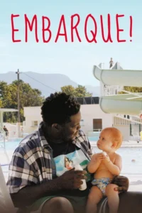 Homem sorridente e bebê ruivo no colo, interagindo em piscina ensolarada com toboáguas e montanhas ao fundo.