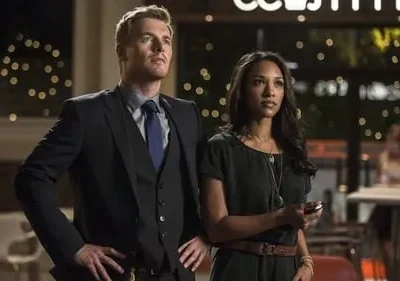 Um homem de terno e uma mulher de vestido olham fixamente para a direita. Fundo noturno com luzes urbanas desfocadas.