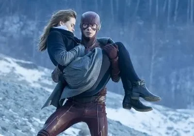 Herói mascarado de vermelho resgata mulher pálida em seus braços, em paisagem gelada e nevada. Clima de perigo e urgência.