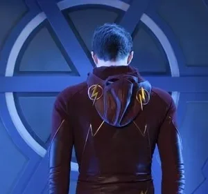 Homem de costas com traje vermelho e raios dourados, em frente a uma imponente porta circular azul de design futurista.