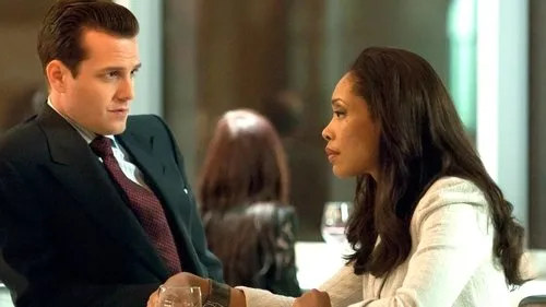Homens de Terno – T01E04:Segredinhos sujos 1 Homem de terno e gravata,e mulher de cabelos longos e blazer claro,trocam olhares sérios num ambiente moderno.
