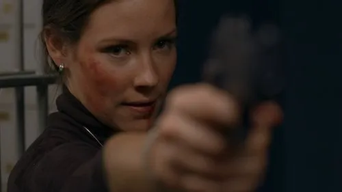 Lost – T01E12:O Que Quer Que Seja 1 Mulher com o rosto ferido e expressão intensa aponta uma arma para a frente. Fundo escuro. Cena de ação e suspense.