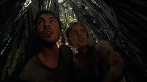 Homem e mulher olham apreensivos para cima,cercados por raízes escuras em uma selva densa. Luz do alto filtra o clima tenso.