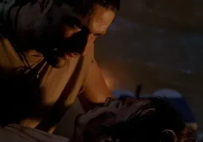 Dois homens em cena escura. Um olha preocupado para o outro deitado, com rosto ensanguentado. Clima tenso e dramático.