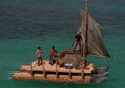 Quatro pessoas em uma jangada improvisada com vela, navegando em águas claras e azuis. Sugere uma jornada ou situação de sobrevivência.