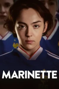 Uma jovem de cabelo curto e castanho, com expressão séria, veste camisa de futebol azul. Outras figuras desfocadas ao fundo.